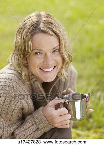 Stock Photo - Woman holding mug outdoors smiling.. Fotosearch