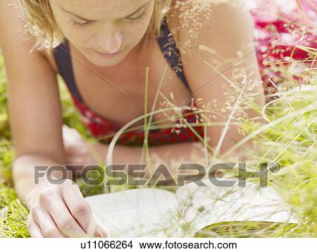 Woman lying in grass reading a book. View Large Photo Image Picture - Woman lying in grass reading a book.. Fotosearch