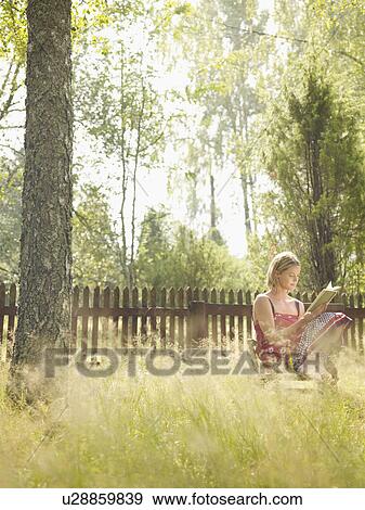 Woman sitting in chair reading by wooden fence. View Large Photo Image Stock Photo - Woman sitting in chair reading by wooden fence.. Fotosearch
