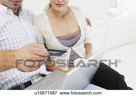 Stock Photo - Couple on sofa, making purchase online. Fotosearch
