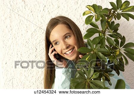 Girl (11-13) using mobile phone behind plant, smiling View Large Photo Image Picture - Girl (11-13) using mobile phone behind plant, smiling. Fotosearch