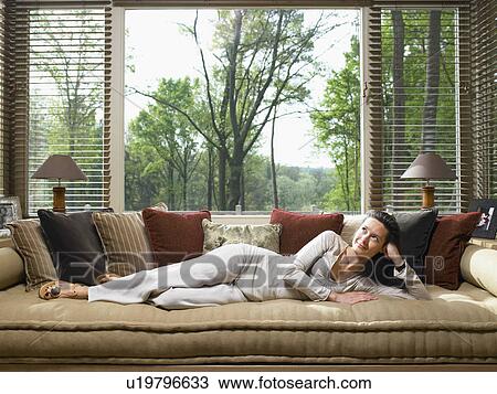 Stock Image - Woman lying on couch in living room smiling and looking up.. Fotosearch