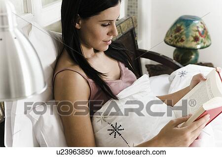 Stock Image - Woman sitting in bed reading.. Fotosearch