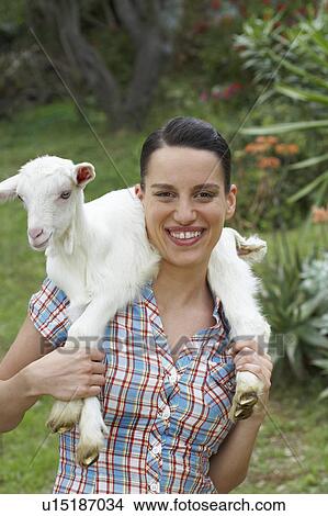 Picture - Young girl with goat on shoulders looking into camera happy.. Fotosearch