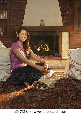 Young woman sitting on rug in front of fire, smiling, portrait View Large Photo Image Picture - Young woman sitting on rug in front of fire, smiling, portrait. Fotosearch