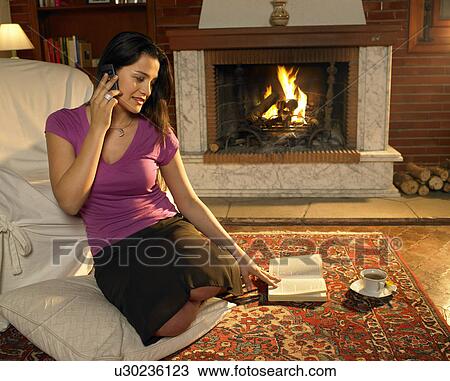 Young woman sitting on rug in front of fire using mobile phone, smiling View Large Photo Image Stock Image - Young woman sitting on rug in front of fire using mobile phone, smiling. Fotosearch