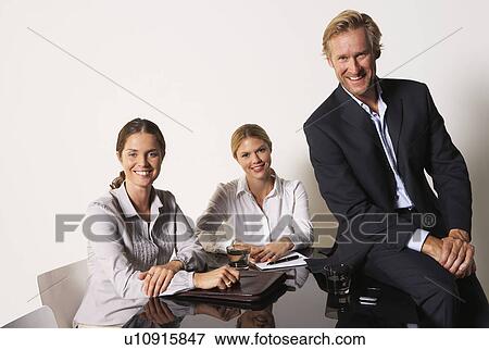Three businesspeople at a table smiling. View Large Photo Image Stock Photo - Three businesspeople at a table smiling.. Fotosearch