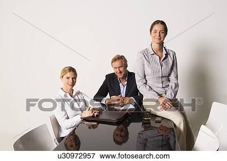 Stock Photo - Three businesspeople at a table smiling.. Fotosearch