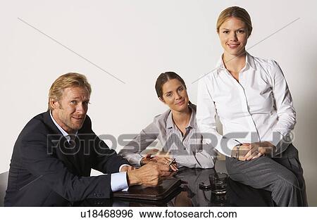 Three businesspeople at a table smiling. View Large Photo Image Stock Photograph - Three businesspeople at a table smiling.. Fotosearch