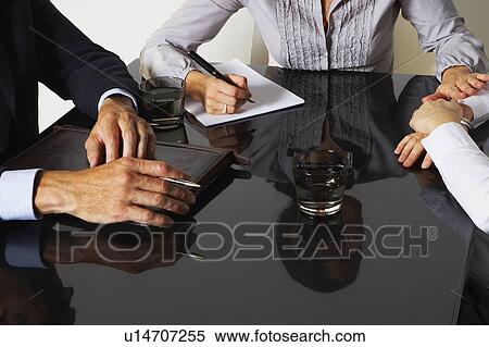 Stock Photography - Three businesspeople with reflections at a table working.. Fotosearch