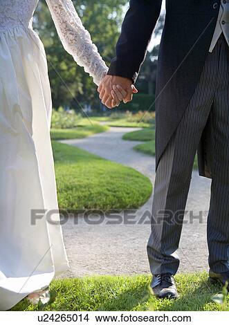 Bride and groom holding hands standing in garden, low section View Large Photo Image Picture - Bride and groom holding hands standing in garden, low section. Fotosearch