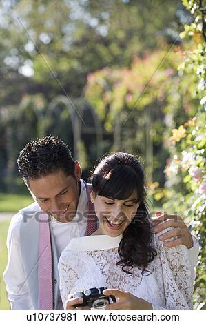 Young bride and groom looking at digital camera in garden, smiling View Large Photo Image Stock Image - Young bride and groom looking at digital camera in garden, smiling. Fotosearch