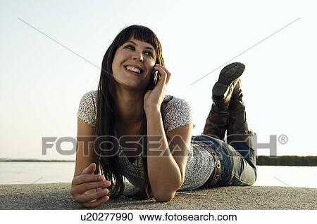 Stock Image - Girl talking on mobile phone by lake.. Fotosearch