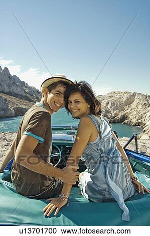 Stock Image - Man and woman sitting on car.. Fotosearch