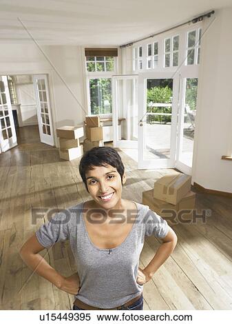 Stock Photography - Portrait of a smiling woman moving in empty house. Boxes in background.. Fotosearch