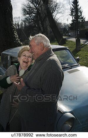 Stock Image - Senior couple leaning on car in countryside, laughing. Fotosearch