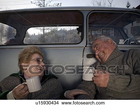 Senior couple sitting by car in countryside, holding cups, smiling View Large Photo Image Picture - Senior couple sitting by car in countryside, holding cups, smiling. Fotosearch