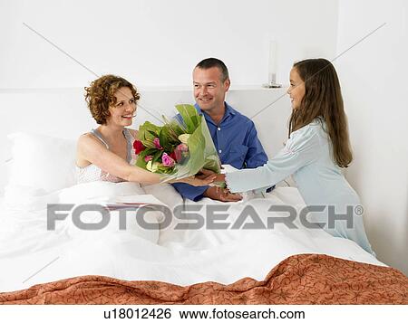 Stock Photograph - Girl giving mother flowers in bed. Fotosearch