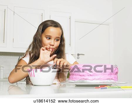 Stock Image - Girl licking finger by iced cake. Fotosearch