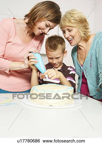Stock Photograph - Grandmother, boy and mom decorating cake. Fotosearch