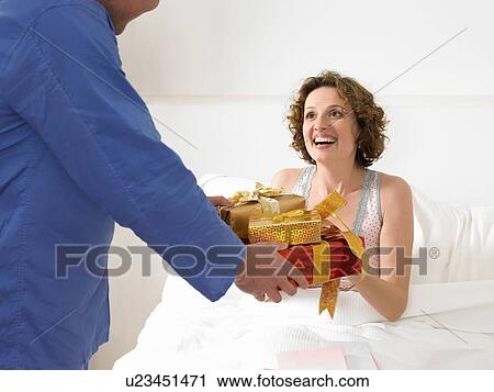 Stock Image - Man handing woman presents in bed. Fotosearch