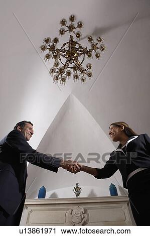 Businessman shaking hands with woman in living room, low angle view View Large Photo Image Stock Image - Businessman shaking hands with woman in living room, low angle view. Fotosearch