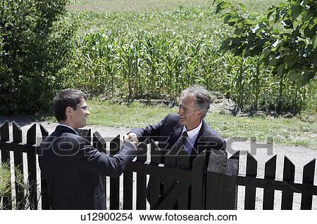 Picture - Businessmen greeting each other over wooden fence.. Fotosearch