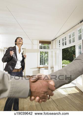 Stock Image - Close up of hand shake with happy woman in background.. Fotosearch