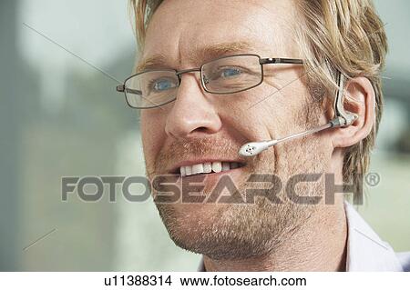 Picture - Close-Up portrait of Businessman using telephone headset / ear piece.. Fotosearch