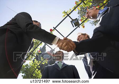Four businessmen shaking hands in a garden View Large Photo Image Stock Photo - Four businessmen shaking hands in a garden. Fotosearch
