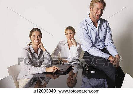Stock Photo - Three businesspeople at a table smiling.. Fotosearch