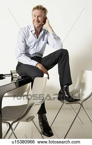 Stock Photograph - Young businessman seated on desk.. Fotosearch