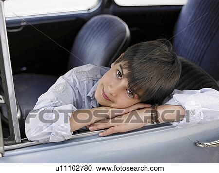 Stock Image - Boy (8-10) sitting in car, leaning out of open window, portrait. Fotosearch