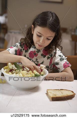 Girl (5-7) eating salad from bowl at a table View Large Photo Image Stock Photography - Girl (5-7) eating salad from bowl at a table. Fotosearch