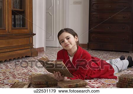 Stock Photo - Girl (9-11) lying on floor reading books, portrait. Fotosearch
