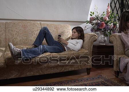 Girl (9-11) lying on sofa holding mobile phone View Large Photo Image Stock Image - Girl (9-11) lying on sofa holding mobile phone. Fotosearch