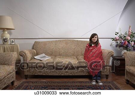 Stock Image - Girl (9-11) sitting on a sofa in a living room, portrait. Fotosearch