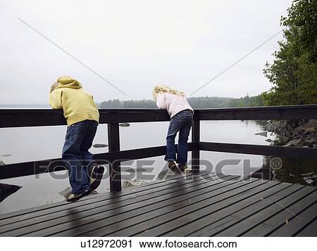Young boy and young girl leaning over a railing by a lake. View Large Photo Image Stock Image - Young boy and young girl leaning over a railing by a lake.. Fotosearch
