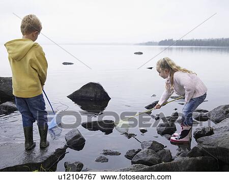 Young boy and young girl on large rocks fishing in a lake with nets. View Large Photo Image Stock Photo - Young boy and young girl on large rocks fishing in a lake with nets.. Fotosearch