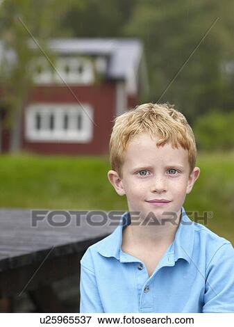 Stock Photo - Young boy sitting at table outdoors with house in background.. Fotosearch