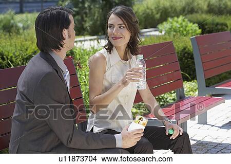 businessman and woman looking at each other with lunch on a bench outdoors View Large Photo Image Picture - businessman and woman looking at each other with lunch on a bench outdoors. Fotosearch
