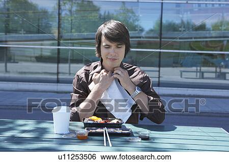 Stock Photograph - Businessman eating sushi outside using napkin.. Fotosearch