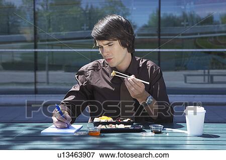 Stock Photo - Businessman eating sushi outside while making notes.. Fotosearch