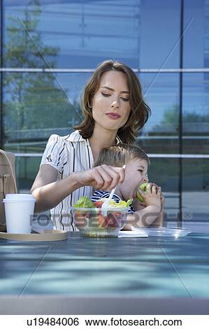 Businesswoman and her son on table in front of office outside she is eating salad to go her son eating apple. View Large Photo Image Stock Photograph - Businesswoman and her son on table in front of office outside she is eating salad to go her son eating apple.. Fotosearch