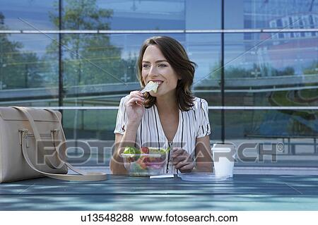 Businesswoman on table in front of office outside biting off salad to go. View Large Photo Image Stock Photo - Businesswoman on table in front of office outside biting off salad to go.. Fotosearch