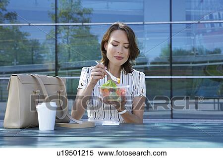 Businesswoman on table in front of office outside eating salad to go laughing. View Large Photo Image Stock Photography - Businesswoman on table in front of office outside eating salad to go laughing.. Fotosearch