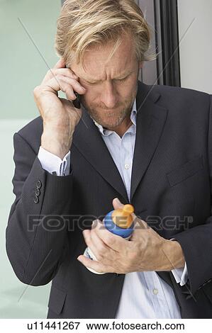 Businessman using mobile phone whilst holding baby's bottle. View Large Photo Image Stock Photo - Businessman using mobile phone whilst holding baby's bottle.. Fotosearch