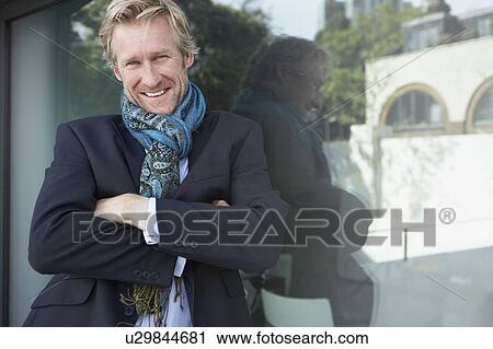Stock Image - Businessman wearing extravagant scarf leaning against window.. Fotosearch