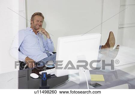 Man at computer smiling relaxing with feet on desk with reflections. View Large Photo Image Stock Image - Man at computer smiling relaxing with feet on desk with reflections.. Fotosearch