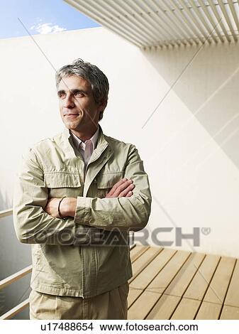 Picture - Man standing on balcony, arms crossed, smiling. Fotosearch